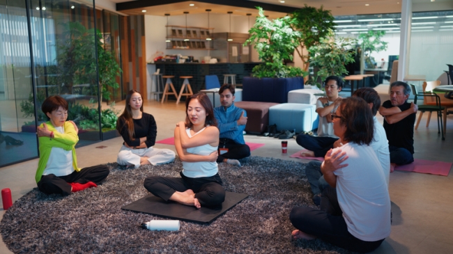 A group of employees sit in a circle, practicing yoga as part of a wellness activity. 