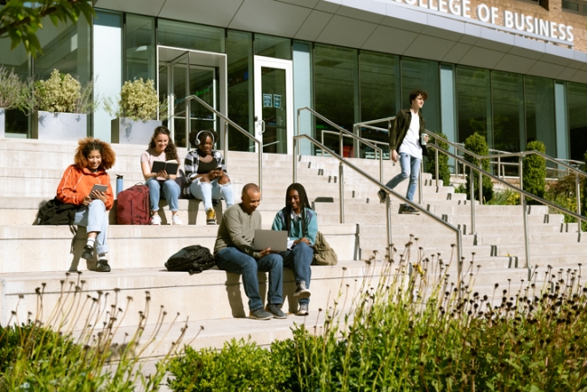 Group of students sitting outside university building in natural environment.