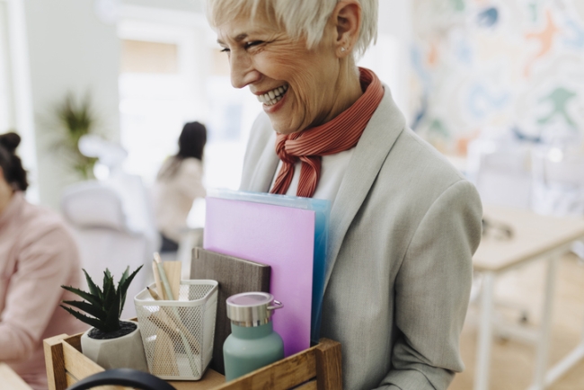 Smiling employee packing personal belongings and saying goodbye to colleagues on her last day.