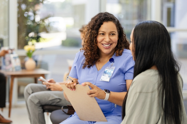 In a clinic lobby, a female patient and smiling nurse talk together.