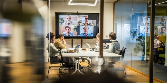 Employees attending a hybrid meeting with some in a conference room and others via video conferencing.