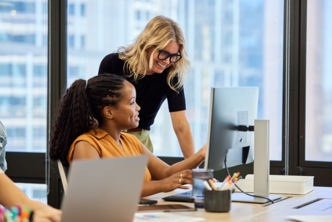 Smiling female I.T. employee helping coworker with their computer. 