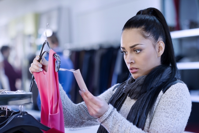 Young woman shocked by price of top in clothing store.