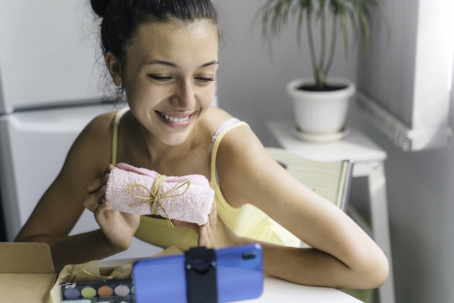 Young woman opening subscription box with bundle of beauty products.