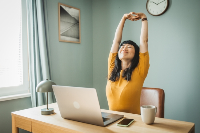 Female employee in yellow sweater stretching at her computer.