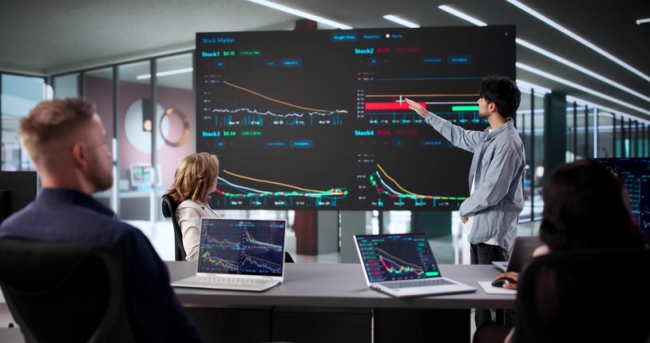 Researchers analyze performance data on a large screen in an office meeting room.