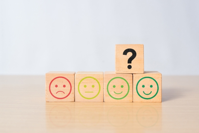 Emoticon rating scale on wooden blocks and a question mark, representing rating scale questions.