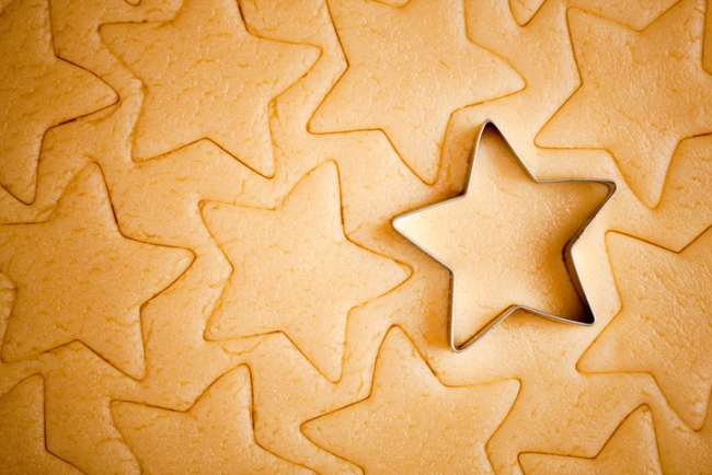 Star shaped Christmas cookies being cut out with cookie cutter.
