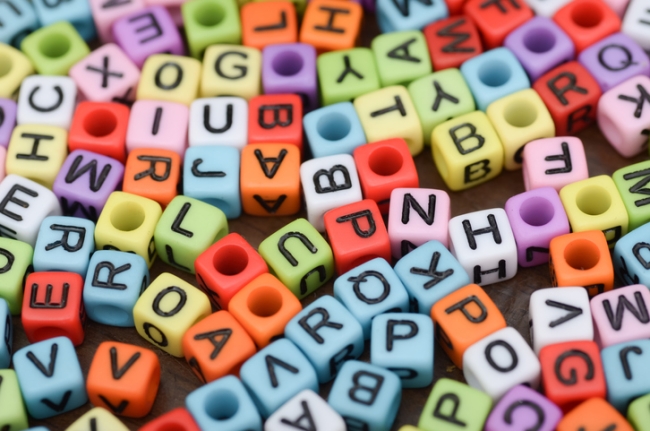 Playful and chaotic mix of multicolored alphabet beads representing randomization.
