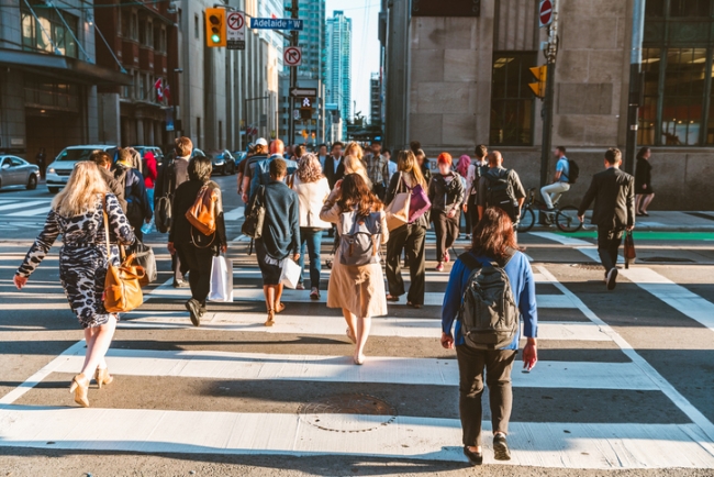 Crowd of unrecognisable people crossing street on traffic light zebra in the city of Toronto at rush hour.