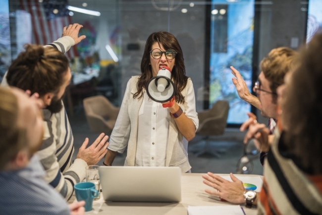 Toxic female leader yelling at her coworkers through megaphone in the office.