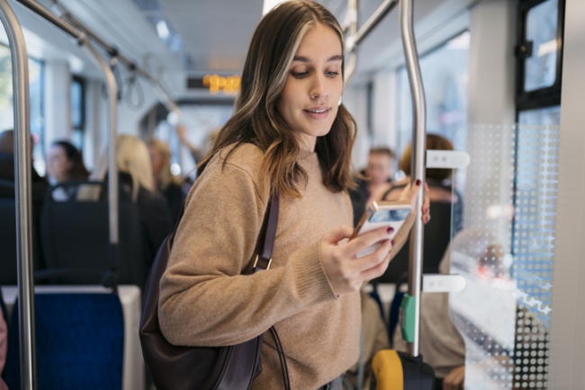 Young woman using smartphone while standing on public transport.