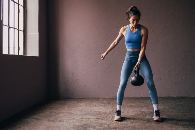 A strong woman in athletic wear lifting a kettlebell, concentrating on her workout.
