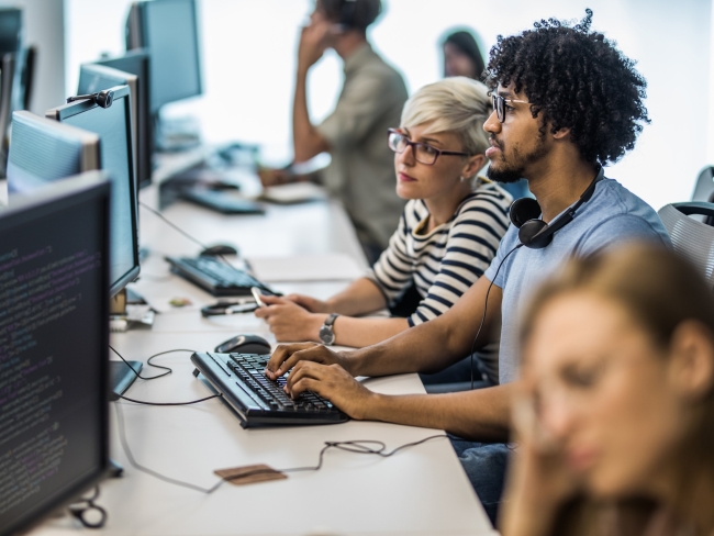 A woman and a man sitting at a desk in an open office review data on a flatscreen monitor