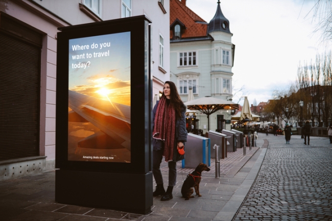 Woman in her late 30s looking at the electronic smart advertisement in the Ljubljana city centre.