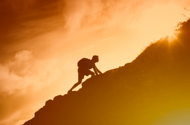 Silhouette of man climbing up a mountain.