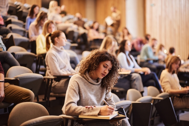 Female college student writing an exam during a class at lecture hall. 