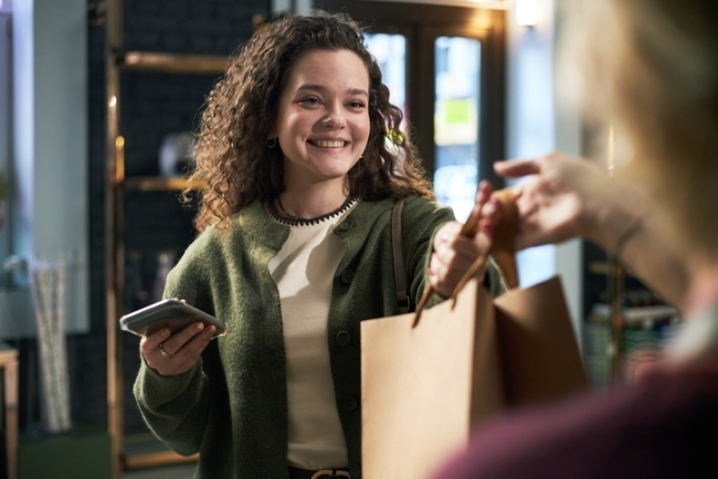 Young woman smiling while receiving purchase in a flower shop following a positive experience.