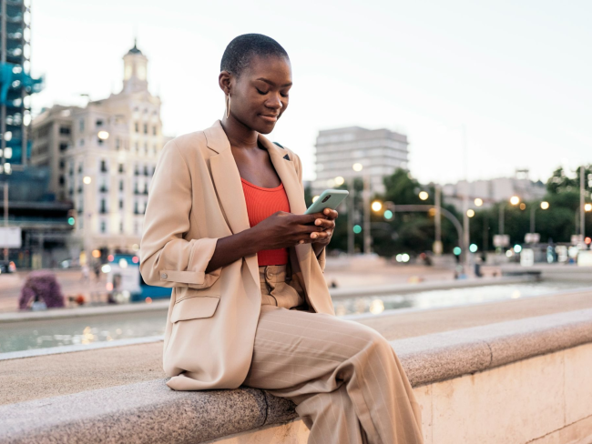 Female US resident sitting on a wall while accessing government services her phone.