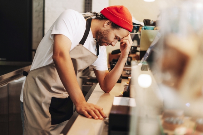 Young barista feeling stressed while working in coffee shop.