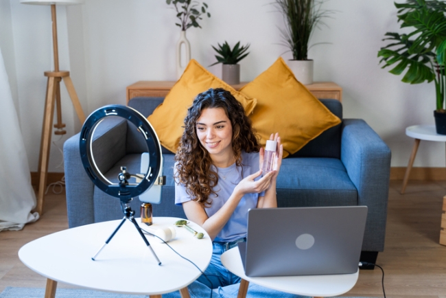 Curly-haired online beauty influencer showcasing skincare products on camera.