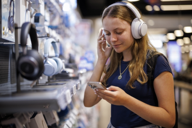 Teenage girl testing headphones in electronics store.