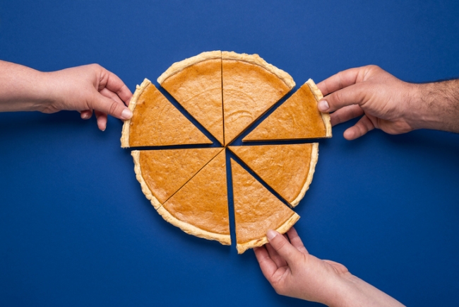 Top view of a home-baked pumpkin pie on a blue background with three people taking a slice.