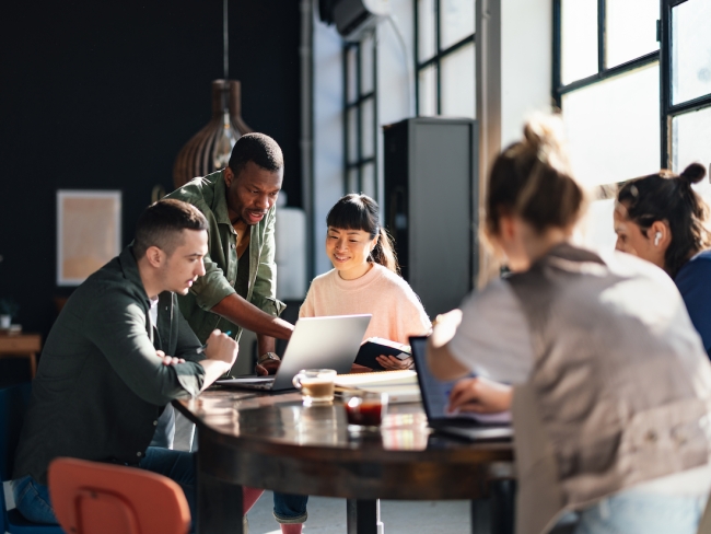 Diverse team collaborating around a laptop at a table in a modern office