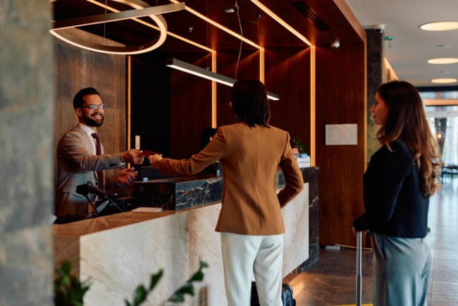 Hotel receptionist hands a key card to a guest at a desk, helping to enhance guest experience.