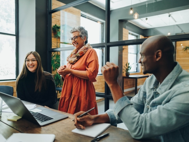 Three colleagues smiling and laughing together during a meeting in a bright modern office