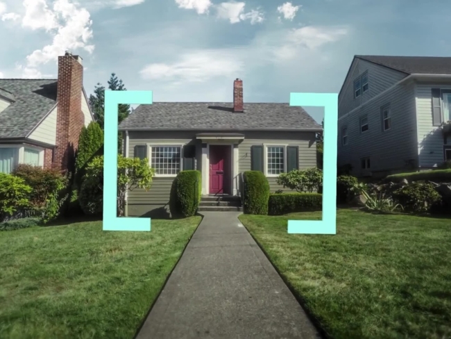 A single-story suburban house with a red door, lawn, and front walkway, all under a blue sky, framed by teal brackets.