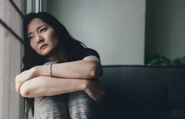Woman in monochromatic clothing curled up, leaning on a window against a gray background