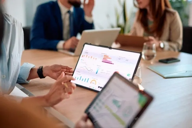 Hands holding tablet with business analytics dashboard showing graphs and charts during team meeting