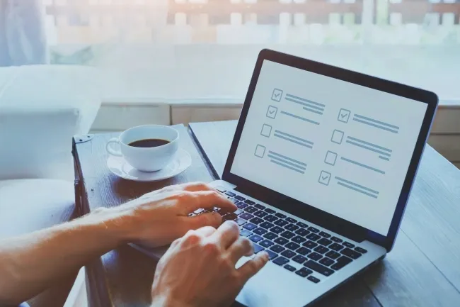 Person typing on laptop with checklist displayed on screen, coffee cup beside keyboard