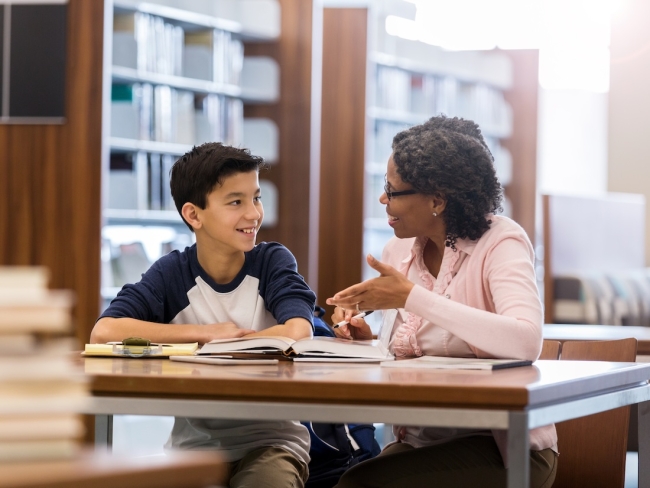 A student and educator talking at a table in a school library