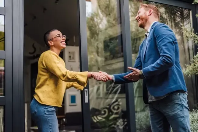 Woman shaking a clients hand outside an office building.
