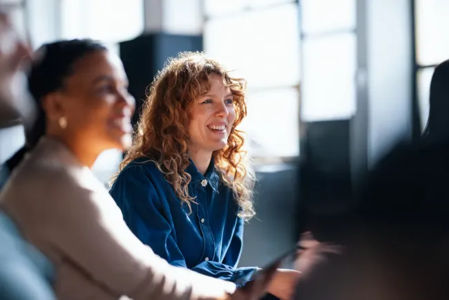 Two cheerful coworkers share ideas in a vibrant office setting, fostering a positive and collaborative workplace atmosphere.