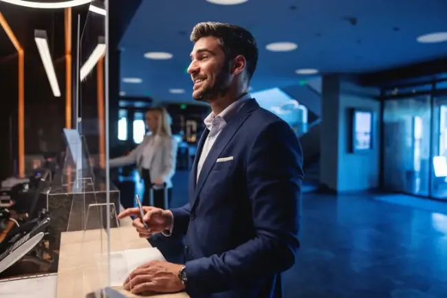 Happy businessman stands at the hotel reception and registers by filling out and signing the form. 