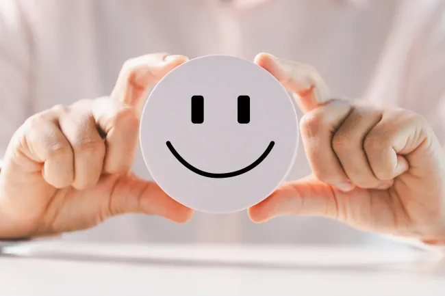 Woman, blurred, holding out an in-focus smiley face. 