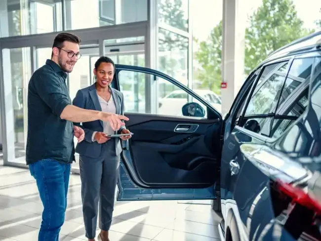 Man in car showroom with sales person looking at a new car