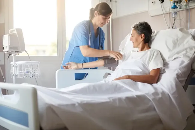 A nurse monitoring the blood pressure of her patient in a hospital bed.
