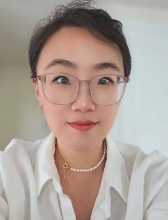 A dark-haired woman with her hair pulled up, smiling warmly, wearing glasses and a white, button-up collared shirt.