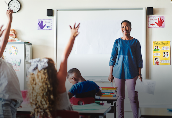 Teacher smiles as her students raise their hands
