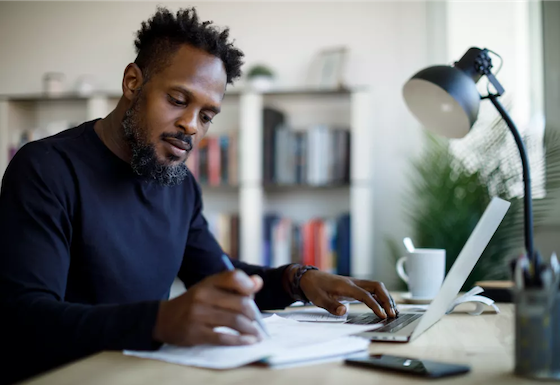 Man working at his desk with his laptop, a notepad, and pen